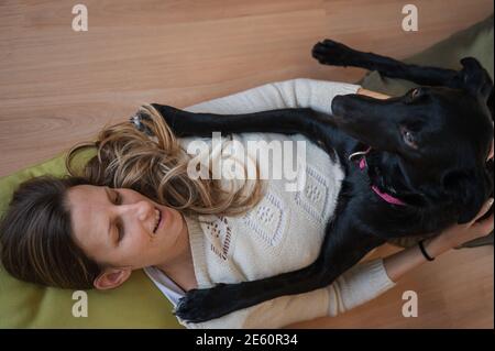 Young woman lying on living room floor with her beautiful black shepherd dog lying on her cuddling. Stock Photo