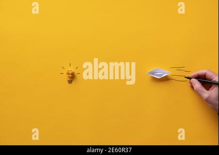 Paper made origami boat floating towards a light bulb made of yellow paper in a conceptual image of vision and idea. Stock Photo