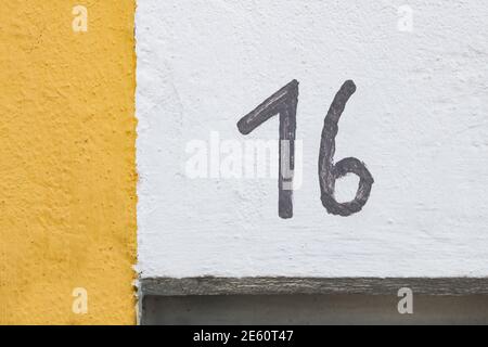 The number 16 roughly hand painted in black on a white wall with a yellow ink strip on the left side of frame. Detail of facade with house number Stock Photo