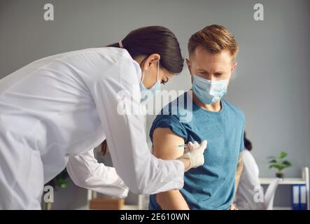 Young female doctor in medical mask injecting vaccine against 19-ncov infection for man patient Stock Photo