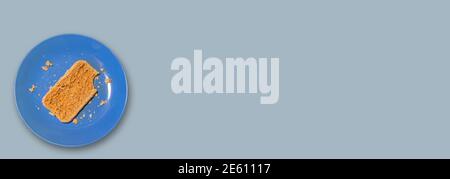 Banner with single piece of bread with a bitten mark lies on a blue plate at solid light blue color background with copy space for text. Concept of po Stock Photo