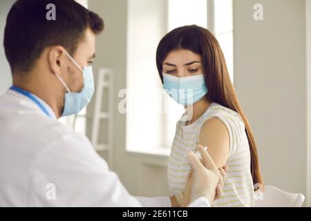 Doctor giving vaccine shot to young woman during immunization campaign at clinic Stock Photo