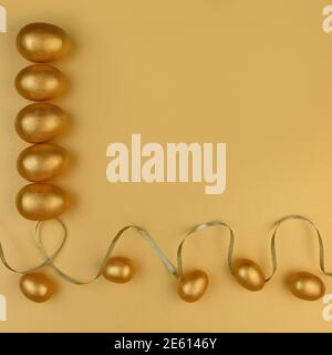 Decorative wooden Easter eggs painted gold on yellow-gold background. Happy Easter greeting card. Stock Photo