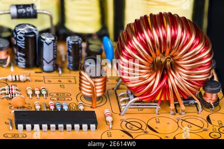 Toroidal or cylindric inductors on printed circuit board. Electronic components. Closeup of magnetic core coils, microchip and resistors on orange PCB. Stock Photo