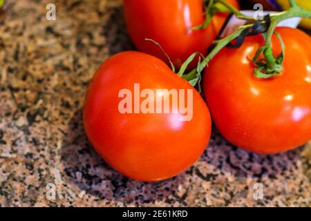 Fresh red tomatoes on the vine seen up close on a granite countertop Stock Photo