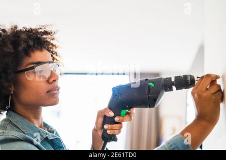 Afro woman drilling wall with electric drill. Stock Photo