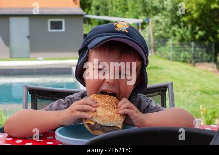 Little boy eating a burger in the garden Stock Photo