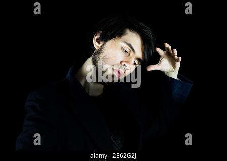Young man looking down with his left hand up doing a pose, with his head and hand being bright Stock Photo