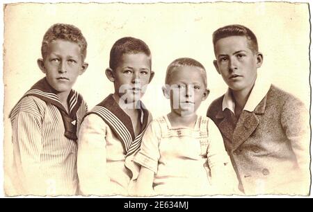 GERMANY - CIRCA 1920s: Vintage photo shows the group of four boys (siblings). Some boys wear sailor costume. Old black and white portrait. 1920s. Stock Photo