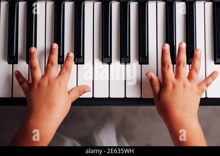 Top view, close-up on two children's hands with fingers spread out as students play on an electronic synthesizer in the living room Stock Photo