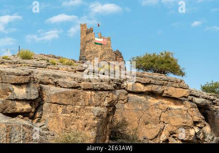 Tower ruins with Omani flag into the hills of the old village Misfat Al Abriyeen, Sultanate of Oman Stock Photo