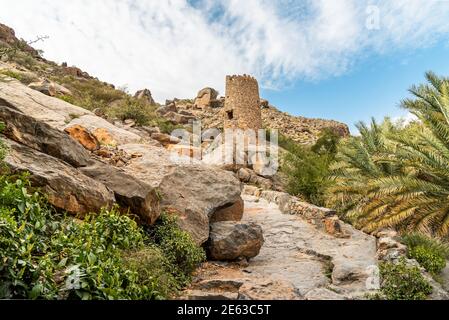 Tower ruins with Omani flag into the hills of the old village Misfat Al Abriyeen, Sultanate of Oman Stock Photo