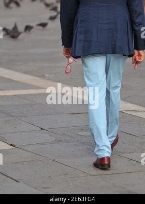 Walking man in dark blue jacket and red glasses in his hand. From behind. Stock Photo