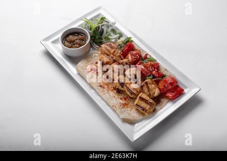Chicken skewers on pita bread with marinated onion sauce and baked bell pepper on a white plate on a white plate Stock Photo