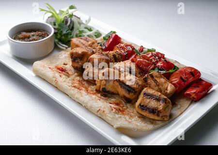 Chicken skewers on pita bread with marinated onion sauce and baked bell pepper on a white plate on a white plate Stock Photo