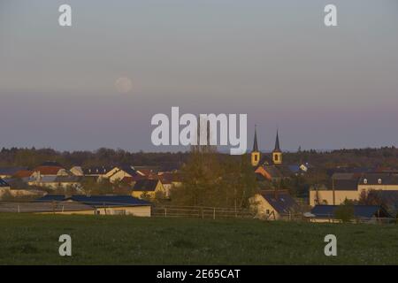 full moon rising over rural countryside outside village and meadow in foreground Stock Photo