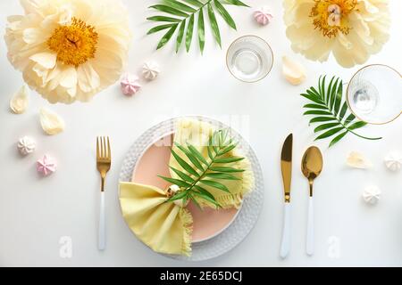 Effortless golden birthday dinner table decor. Pale yellow peony flowers. White dinner table, white and gold utensils, decorated with season flowers Stock Photo