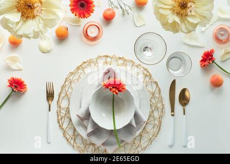Effortless golden birthday dinner table decor. Summer flat lay. White dinner table, white and gold utensils, decorated with peony flowers, orange Stock Photo