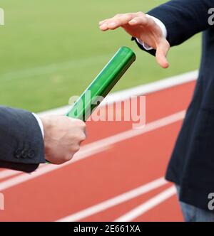 Businessmen pass on the baton in relay race in stadium Stock Photo