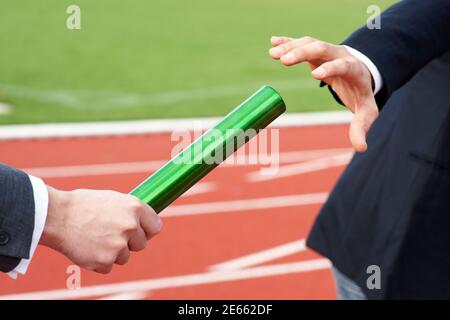 Businessmen pass on the baton in relay race in stadium Stock Photo