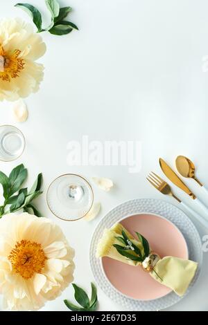 Effortless golden birthday dinner table decor. Pale yellow peony flowers. White dinner table, white and gold utensils, decorated with season flowers Stock Photo
