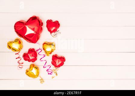 Seven metallic shiny balloons in the form of heart. One big red shiny balloon in the shape of a heart and six small heart-shaped balloons in gold and red colors with ribbons lie on wooden beige boards. Valentine's Day. The 14th of February concept. banner with copyspace. place for text. flatlay Stock Photo