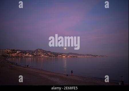 Malaga, Spain. 28th Jan, 2021. The wolf moon seen rising over the horizon as people enjoy the good weather at Malagueta beach.During the first month of the year “Wolf moon “takes place. This year will observe other two sun and lunar eclipses and three supermoon. Credit: SOPA Images Limited/Alamy Live News Stock Photo