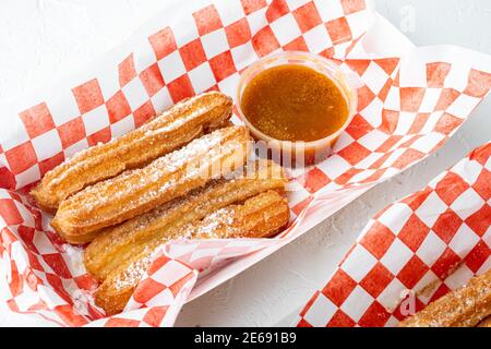 Tasty hot sweet churros in paper with chocolate, and caramel in paper tray, on white background Stock Photo