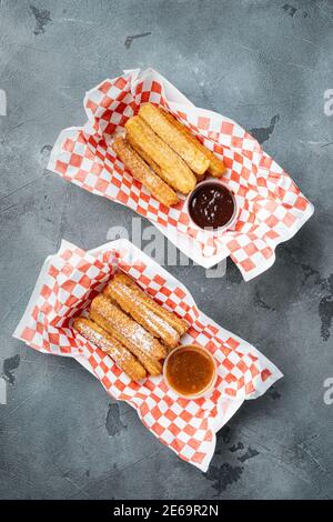 Tasty hot sweet churros in paper with chocolate and caramel in paper tray, on gray background, top view flat lay Stock Photo