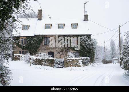 Country road and cotswold stone cottage in Swinbrook in the snow. Swinbrook, Cotswolds, Oxfordshire, England Stock Photo