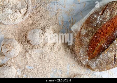 Flat lay image of a homemade sourdough bread loaf cooling on a napkin on marble countertop where other hand rounded dough are sitting in flour with ad Stock Photo