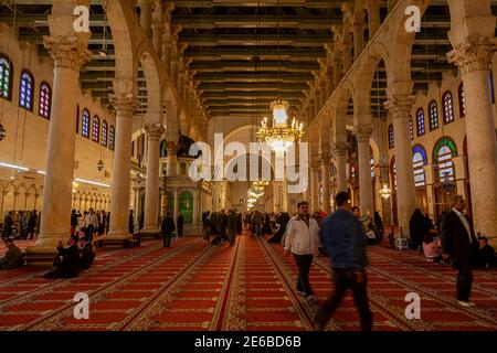 Damascus, Syria 03-27-2010: Inside of the famous Umayyad Mosque where muslim men have gathered for worshiping on the main carpeted hall. There are dec Stock Photo