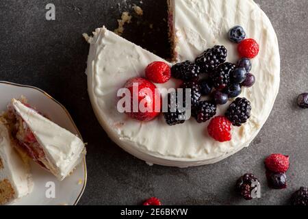Close up image of a round cake with creamy white icing and assortment of berries used as decorative toppings. Served On dark gray black background. Tw Stock Photo