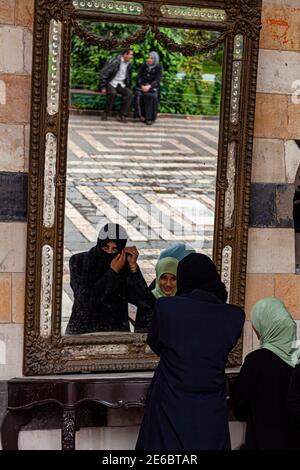 Damascus, Syria 03-28-2010: A young arabic woman is standing in front of a mirror putting on niqab mouth cover under her hijab. This is a religious ou Stock Photo