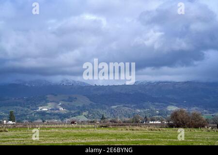 Dusting of snow covers hills beyond a grass field after a cold winter storm in January 2021 in Sonoma County, California. Stock Photo