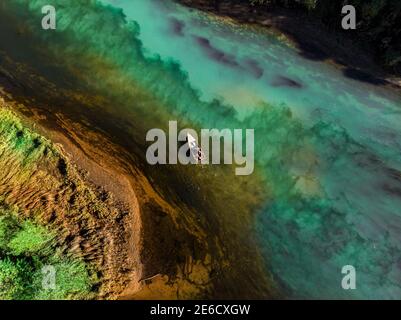 An overhead view of a motor boat sails against the current on a colored blue-green river. Aerial drone shooting Stock Photo