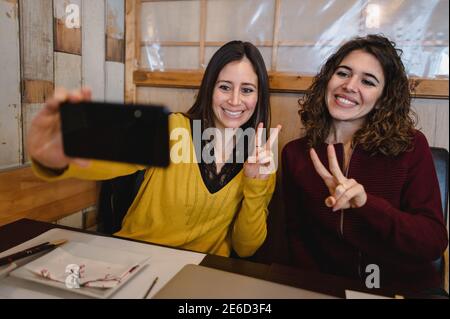 Two Hispanic women with peace sign selfies using a mobile phone in a restaurant Stock Photo