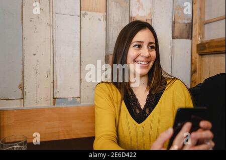 Smiling Hispanic woman using her phone at a restaurant Stock Photo