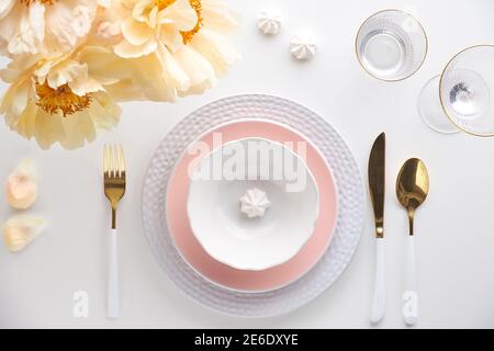 Effortless golden birthday dinner table decor. Pale yellow peony flowers and Late Spring, Summer flat lay. White dinner table, white, gold utensils Stock Photo
