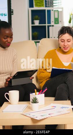 Friendly creative diverse colleagues team discussing about online project using laptop and tablet at workplace. Multiracial coworkers group working together sharing marketing ideas at office meeting Stock Photo