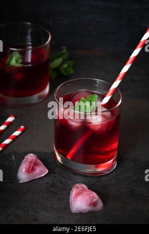 Cherry cocktail with heart shaped ice cubes on a dark background.