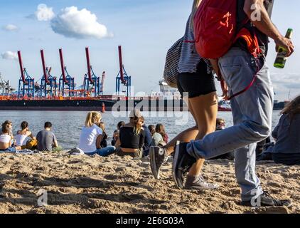 Locals and tourists relaxing in the sun on the sandy Elbstrand beach on the River Elbe opposite Hamburg docks in Germany Stock Photo