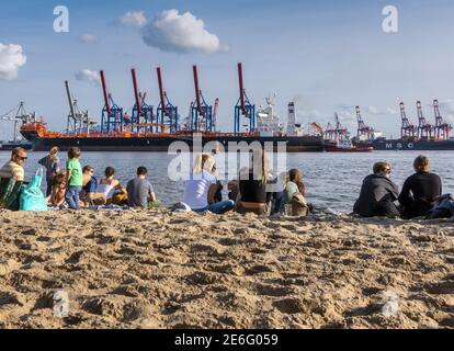 Locals and tourists relaxing in the sun on the sandy Elbstrand beach on the River Elbe opposite Hamburg docks in Germany Stock Photo