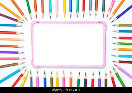Children's digital tablet on a white table with a frame of colored pencils for drawing Stock Photo