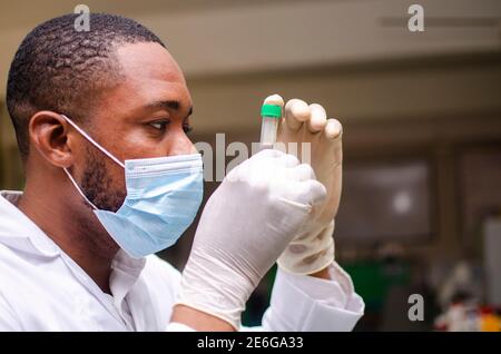 Young black lab scientist wearing a nose mask, observing a blood sample in his hand Stock Photo