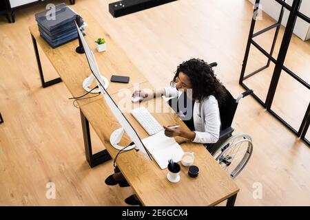 Disabled African Worker In Wheelchair Working On Computer Stock Photo