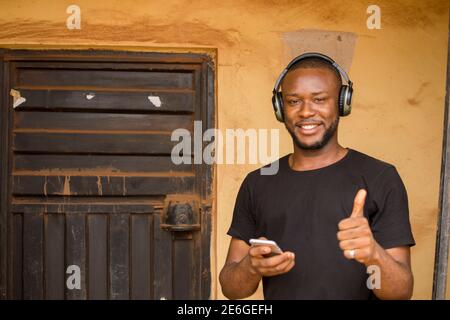 young black man standing outside, using his wireless headphone to listen to songs on his phone Stock Photo
