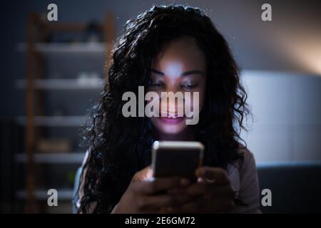 African Woman Using Mobile Phone Or Smartphone In Dark At Night Stock Photo