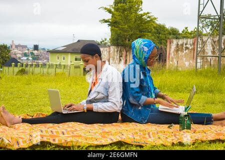 young beautiful black ladies sitting outside, using their laptops and catching fun Stock Photo