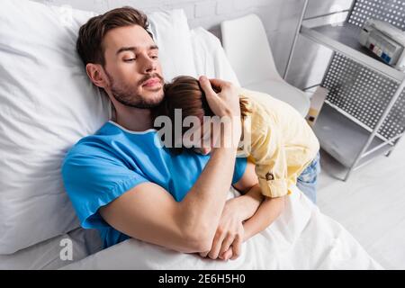 ill man embracing daughter while lying in hospital bed Stock Photo